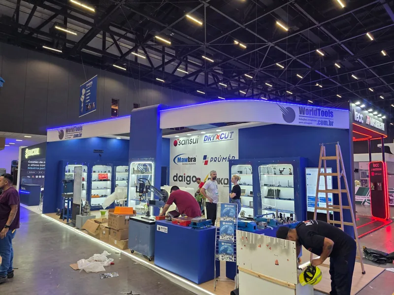 Bastidores da montagem do estande da World Tools na Feimec 2026, com operários, escada e vitrines ainda em instalação